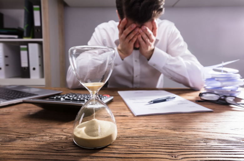 Business man with head in hands on desk, frutrated about tax time and time running out