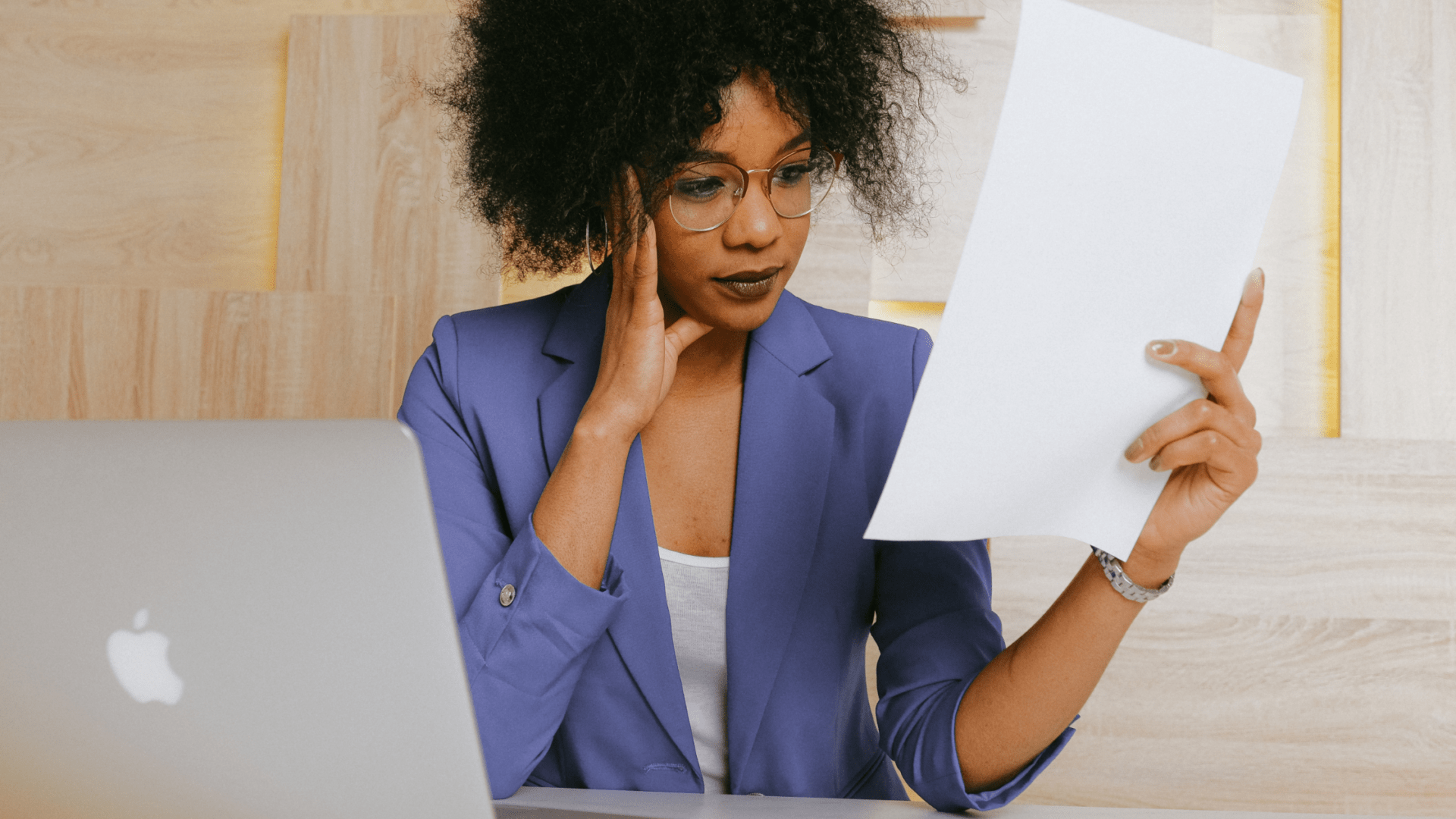 Founder of small business is looking at a piece of paper while sitting at a desk in front of her laptop