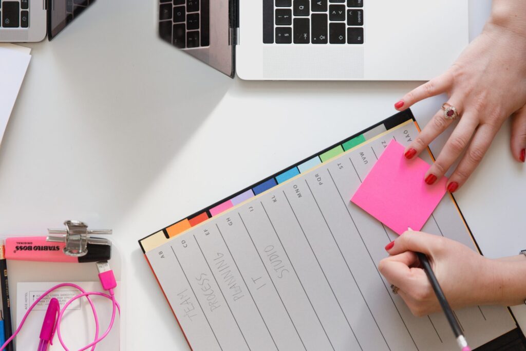 A woman's hands about to write something on a sticky note, on top of a paper productivity tool.